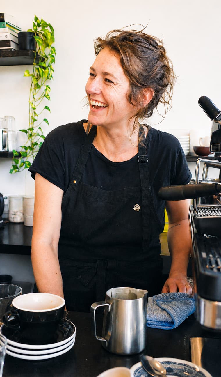 A barista laughing behind the espresso machine in a cafe